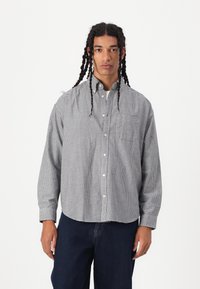 Sjekk skjorte i marineblå og hvit, blanding av bomull, lange ermer, brystlomme og knappefeste ved håndleddene. Kombinert med mørke denimjeans.