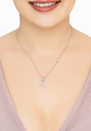 Silver necklace featuring a curvy pendant adorned with small clear stones and a round stone accent, displayed against soft fabric.
