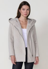 Beige kapucnis kabát strukturált gallérral, textúrált anyagból és átlós bordákkal. Cipzáros záródással és oldalsó zsebekkel rendelkezik.