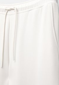 Primo piano di pantaloni della tuta bianchi con fascia elastica in vita e coulisse, dotati di tasca laterale e tessuto morbido.