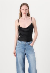 Juoda satino camisole su cowl apykakle ir plonomis spaghetti petnešomis, derinama su šviesiai mėlynomis aukšto liemens plačiomis kelnėmis.
