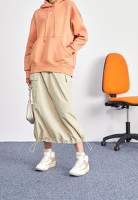 Orange hoodie med framficka och dragsnören, beige verktygsrock med elastisk nederdel och vita sneakers med beige accenter.