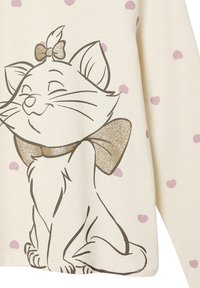 Helle beige Langarmbluse mit einem Cartoon-Katzen-Design, ausgestattet mit einem goldenen Glitzerband und weißen Punkten in zartem Rosa.