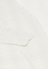 Bílá pletená látka s otevřeným vzorem. Měkká textura, mírně splývavá, s jemnou vazbou a bezšvými okraji.