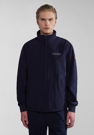 Marinblå jacka med ståkrage, framzipper, sidofickor och logodetalj på bröstet. Tillverkad av lättviktig tyg med en slät yta.
