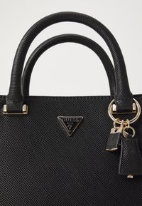 Black handbag featuring textured material, dual handles, gold-tone hardware, and a triangular logo plate. Keychain accents complete the design.