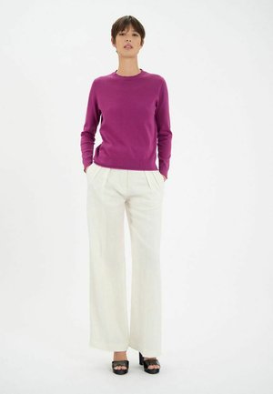 Pull en maille fuchsia avec un col rond, associé à un pantalon large taille haute crème et des sandales à plateforme noires. Fond uni.