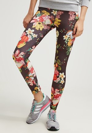 Personne portant des leggings foncés avec un imprimé coloré de fleurs et de fruits, un sweat-shirt gris et des chaussures de course grises avec des rayures blanches.