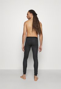 Schwarze, enganliegende Leggings mit glatter Textur und elastischem Bund, von hinten getragen, die ein schmal zulaufendes Design zeigen.