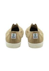 Beige vászon slip-on cipő kerek orral, fehér gumitalppal és logó folttal a sarkán, látható varrási részletekkel.