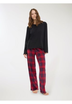 Top a maniche lunghe nera con collo a giro e pantaloni a quadri rossi caratterizzati da una vestibilità ampia e un tessuto morbido. Modella è a piedi nudi.