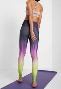 Legginsy z wysokim stanem przechodzące od ciemnoszarego przez różowy do zielonego, z pionowymi paskami i gładkim, elastycznym materiałem.