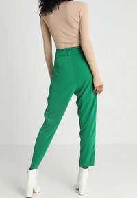 Beige žebrovaný dlouhý rukáv top, spárovaný s vysokými zelenými kalhotami se bočními kapsami a zúženými nohavicemi, doplněný bílými lodičkami na podpatku.