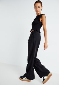 Čierny priliehavý crop top s volánovým lemom, skombinovaný s vysokými čiernymi širokými nohavicami a námorníckymi teniskami s bielymi pruhmi a gumovou podrážkou.