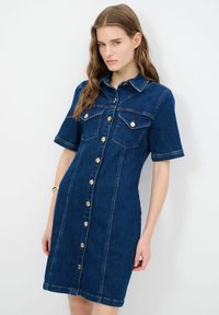 Kankari mekko tummansinisessä värissä, jossa on lyhyet hihat, napit edessä, kaksi rintataskua, kultasävytetyt napit ja ommellut yksityiskohdat.