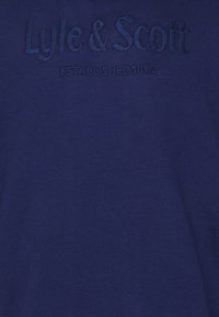 Tessuto blu scuro con testo ricamato in rilievo "Lyle & Scott" sopra "FONDATO NEL 1874" in filo blu abbinato.
