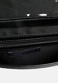 Borsa di stoffa nera con una texture liscia, dotata di un compartimento con zip e un'etichetta interna che dice "M&S Collection."