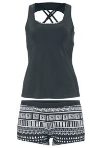 Top tankini nero con spalline incrociate, abbinato a pantaloni da bagno a righe bianche e nere con design geometrici e una texture morbida.