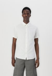 Short-sleeve white button-up shirt made of lightweight fabric, featuring a standard collar and clear button closure, paired with grey cargo shorts.