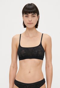 Črn bralette z tankimi naramnicami, oblikovan iz prozorne tkanine s subtilnim vzorcem listov in enotnim črnim pasom na dnu.