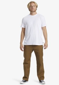 Weißes T-Shirt mit kurzen Ärmeln, braune gerade Hosen, schwarz-weiße Sneakers. Minimalistisches Design, normale Passform, glatte Textur.