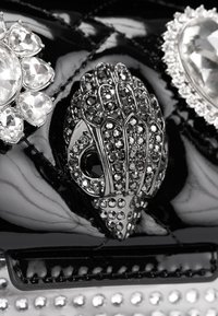 Schwarze Handtasche aus Lackleder mit metallischen Akzenten, großen Edelsteinen und filigranen Verzierungen, einschließlich eines dekorativen Handdesigns.