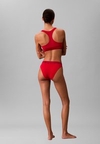 Reggiseno sportivo rosso e mutandine coordinate in tessuto morbido, con design a schiena scoperta e dettagli del logo sull'elastico.