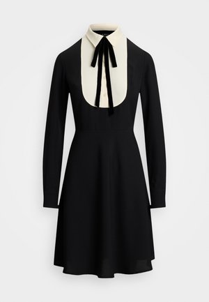 Vestido negro de manga larga con cuello bib blanco y pajarita de terciopelo negra, cintura ajustada y falda acampanada.