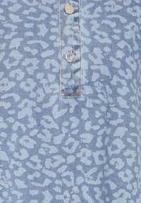 Tissu en denim avec imprimé léopard bleu clair et boutons-pression métalliques sur une patte cousue.