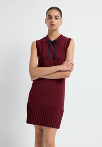 Abito senza maniche color bordeaux con colletto, arricchito da un papillon blu navy e un orlo pieghettato. Tessuto liscio con dettagli decorativi a contrasto.