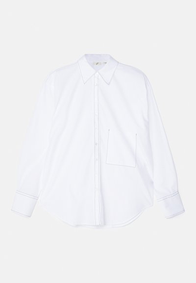 Cămașă albă cu mâneci lungi, fabricată dintr-un material neted, având un gât cu nasturi, guler mare, margine rotunjită și o singură buză pe partea stângă a pieptului, cu detalii de cusătură.