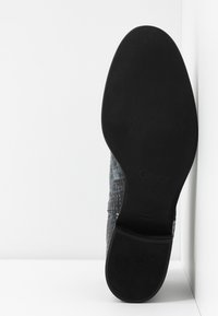 Suela de zapato negra con superficie de goma texturizada; presenta una parte superior suave con un acabado sutil y decorado; logotipo del fabricante visible.