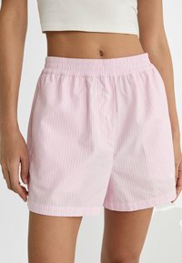 Gros plan sur une personne portant un short élastique à taille rose clair et blanc rayé avec deux boutons à l'avant et un haut court blanc.