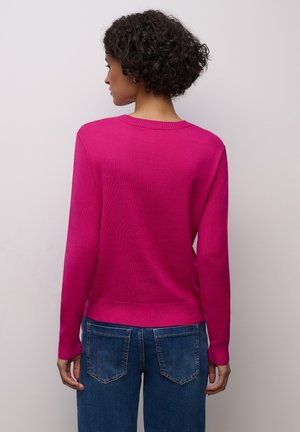 Pull tricot fuchsia avec un col rond, des manches longues et des bordures côtelées, associé à un jean en denim bleu. Texture lisse, coupe ajustée.