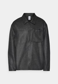 Veste chemise noire texturée avec un col, des manches longues et une poche avant ; dotée d'une poche zippée et d'un motif subtil sur le tissu.