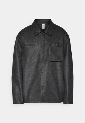Black textured shirt jacket with a collar, long sleeves, and front pocket; features a zip pocket and a subtle pattern on the fabric.