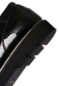 Tacón de zapato de cuero negro brillante con suela gruesa de goma negra acanalada y costuras visibles en el lado superior.