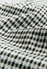 Textil med ett hounds-tooth-mönster i svart och brunt på en vit bakgrund, med en mjuk, slät textur och viss drapering.