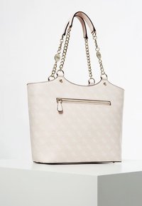 Jasnoróżowa torba na ramię wykonana z teksturowanego materiału, z przednią kieszenią na zamek, złotymi łańcuszkami na ramiączkach oraz subtelnym wzorem logo.