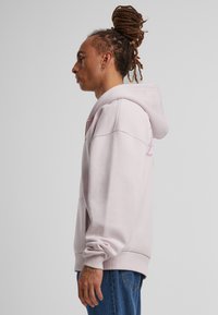 Felpa rosa chiaro con vestibilità comoda, grande cappuccio e tasca frontale. Tessuto morbido, polsini e orlo a costine. Presenta un branding discreto sul petto.