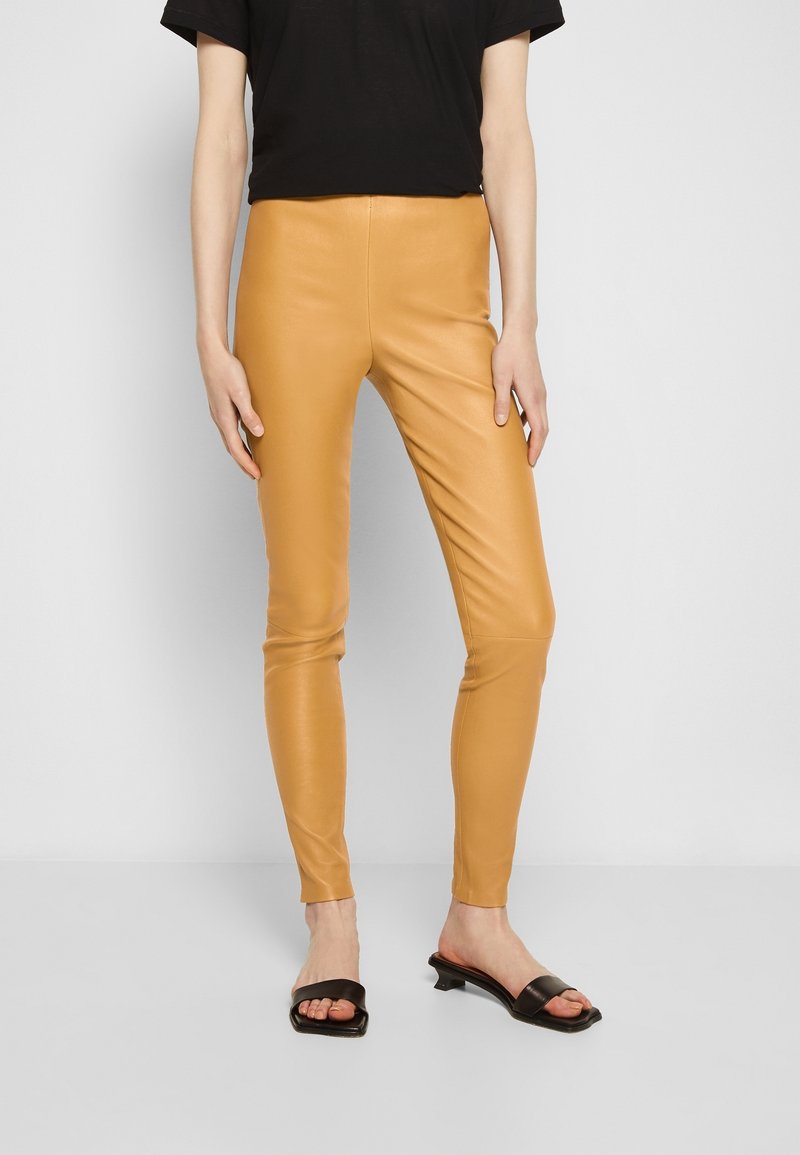 Legging en simili cuir, taille haute et coupe ajustée, en jaune moutarde. Texture lisse avec des coutures minimales. Associé à un haut noir à manches courtes.