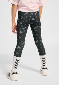 Svarta leggings med ett upprepat grått logomönster, kombinerat med vita strumpor med svarta zigzag-mönster och vita sneakers.