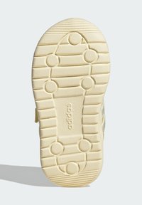 Light yellow rubber shoe sole with textured tread, circular grip patterns, and brand logo "adidas" embossed along the center line.