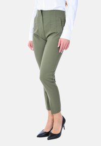 Pantaloni verdi oliva a vita alta, sartoriali, con dettagli a righe verticali, tasche e orlo lungo la caviglia, abbinati a tacchi a punta neri.