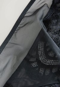 Melns mežģīņu audums ar sarežģītām rakstām, ar gludu pelēku odere un caurspīdīgu tekstūru. Malas ir nostiprinātas ar drošu šuvi.