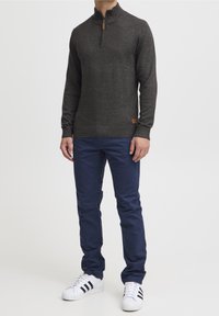 Tummanharmaa neulottu pusero, jossa on korkea kaulus ja vetoketju, yhdistetty laivastonsinisiin housuihin ja valkoisiin lenkkareihin, joissa on mustat raidat.