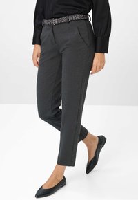 Graue, taillierte Hose mit Fronttaschen, schmal zulaufenden Beinen und einer dezenten Textur, kombiniert mit einem schwarzen flachen Schuh und einem gemusterten Gürtel.