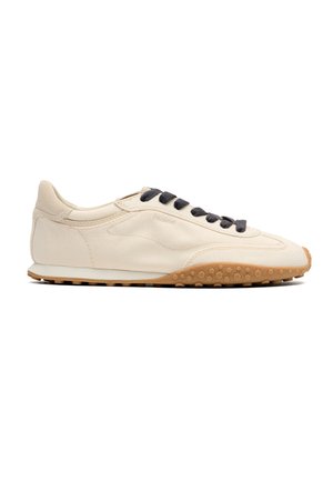 Sneaker beige low-top con lacci neri e suola in gomma marrone testurizzata, con cuciture minimaliste e branding laterale discreto.