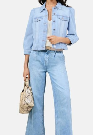 Kvinde iført en lyseblå denimjakke og høj-taljede vidde-jeans, der holder en beige håndtaske med slangeskindsprint.