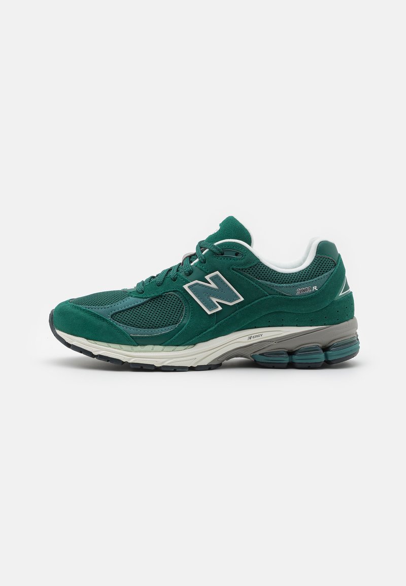 Green suede and mesh sneaker with a cushioned sole and silver logo. Features rounded toe and lace-up design, with a textured finish.